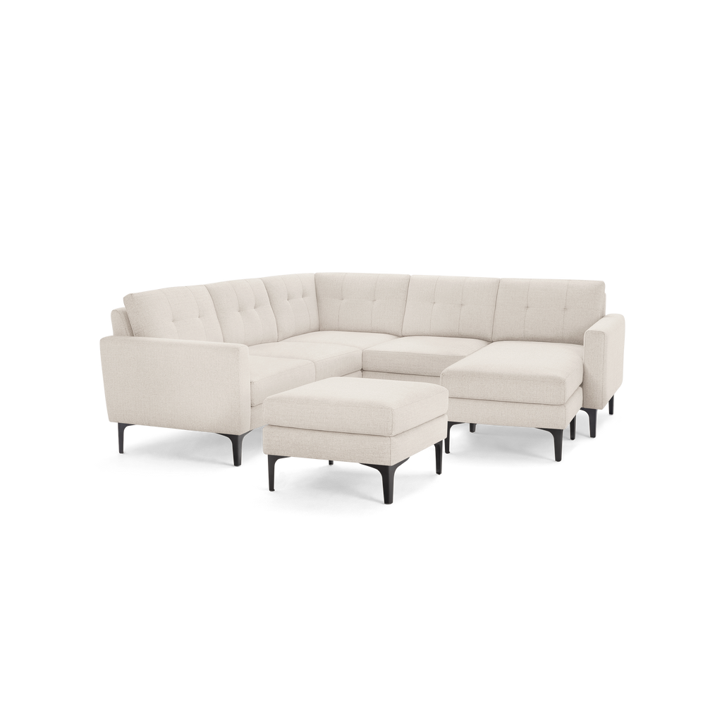 Cream-colored upholstered L-shaped sectional sofa with tufted cushions and matching ottoman, featuring sleek black legs.