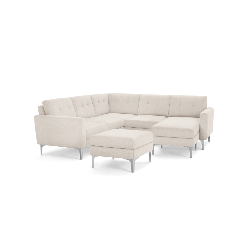 Cream-colored L-shaped sectional sofa with tufted back cushions and matching ottoman, featuring sleek metal legs.