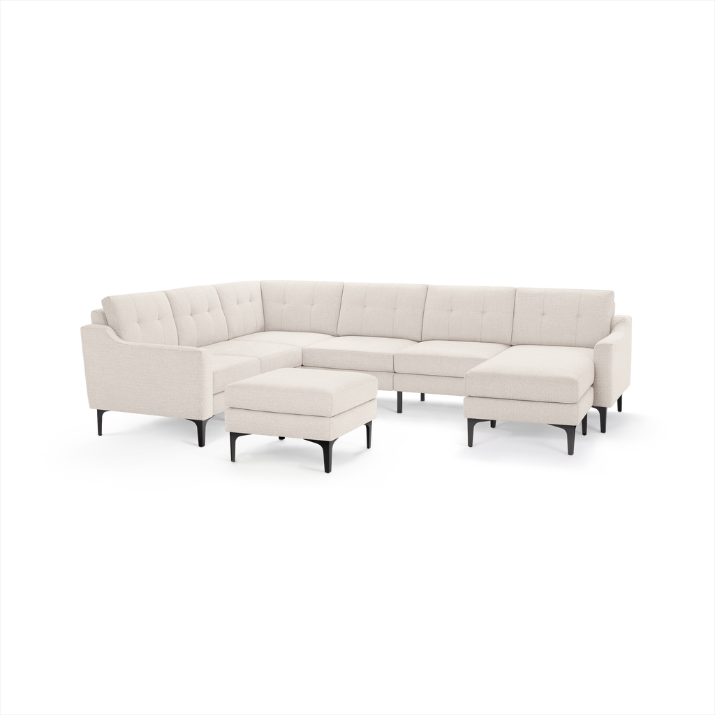Modern L-shaped beige fabric sectional sofa with tufted back cushions and matching ottoman on black legs.