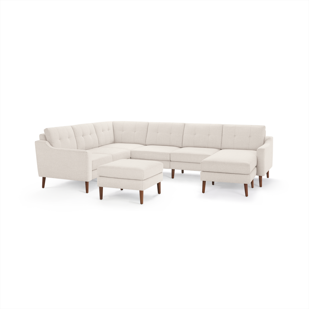 Beige fabric sectional sofa with tufted back cushions, wooden legs, and matching ottoman on a white background.
