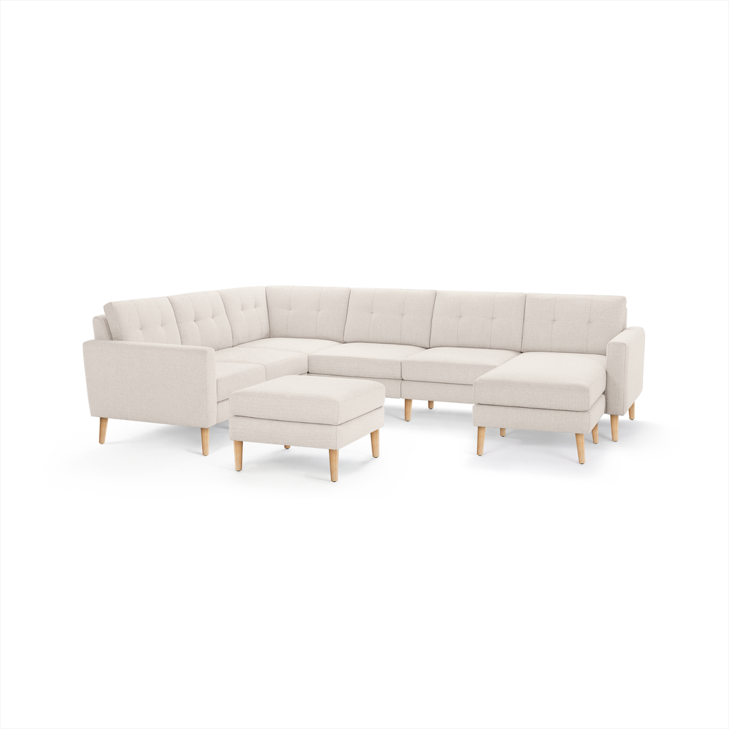 Beige fabric L-shaped sectional sofa with tufted back cushions, wooden legs, and matching ottoman, modern minimalist design.