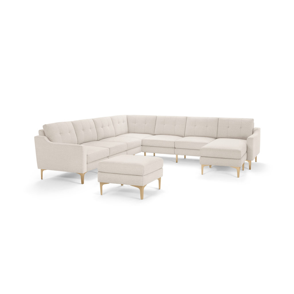 Modern large beige L-shaped sectional sofa with tufted cushions and matching ottoman, supported by light wooden legs.