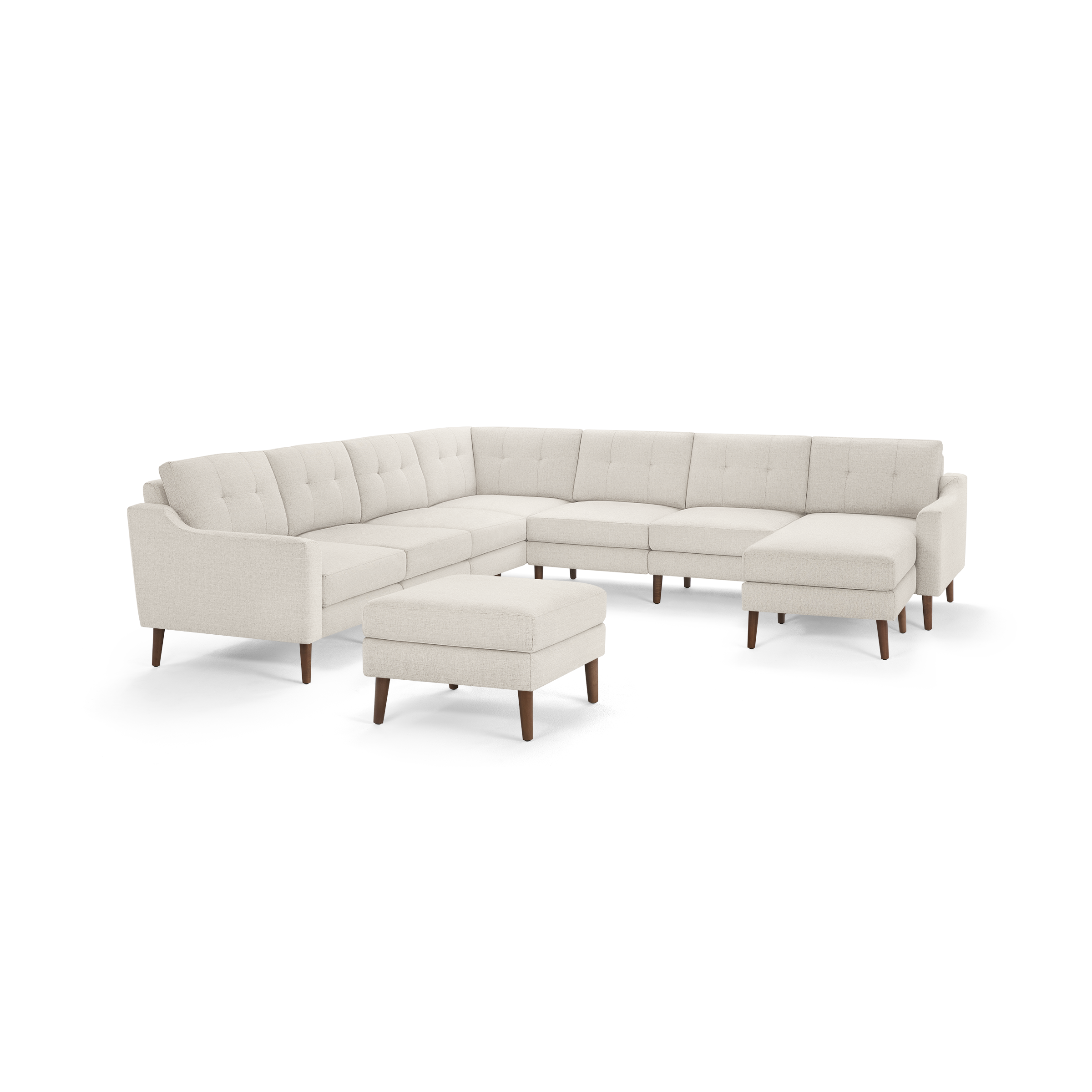 Large beige fabric sectional sofa with tufted back cushions and wooden legs, accompanied by a matching ottoman.