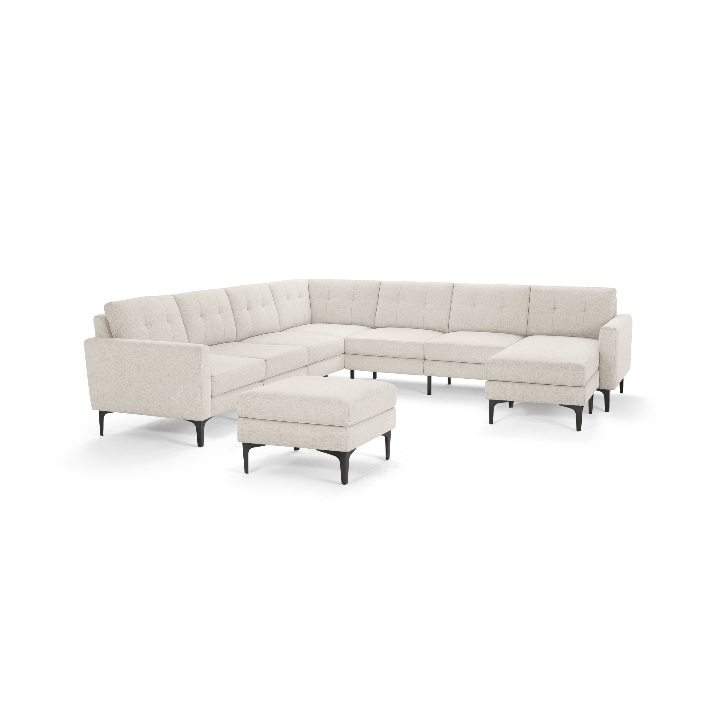 Large L-shaped beige fabric sectional sofa with tufted back cushions, matching ottoman, and slim black legs.