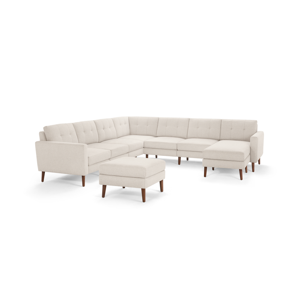 Cream-colored large sectional sofa with tufted back cushions and matching ottoman, featuring wooden legs.