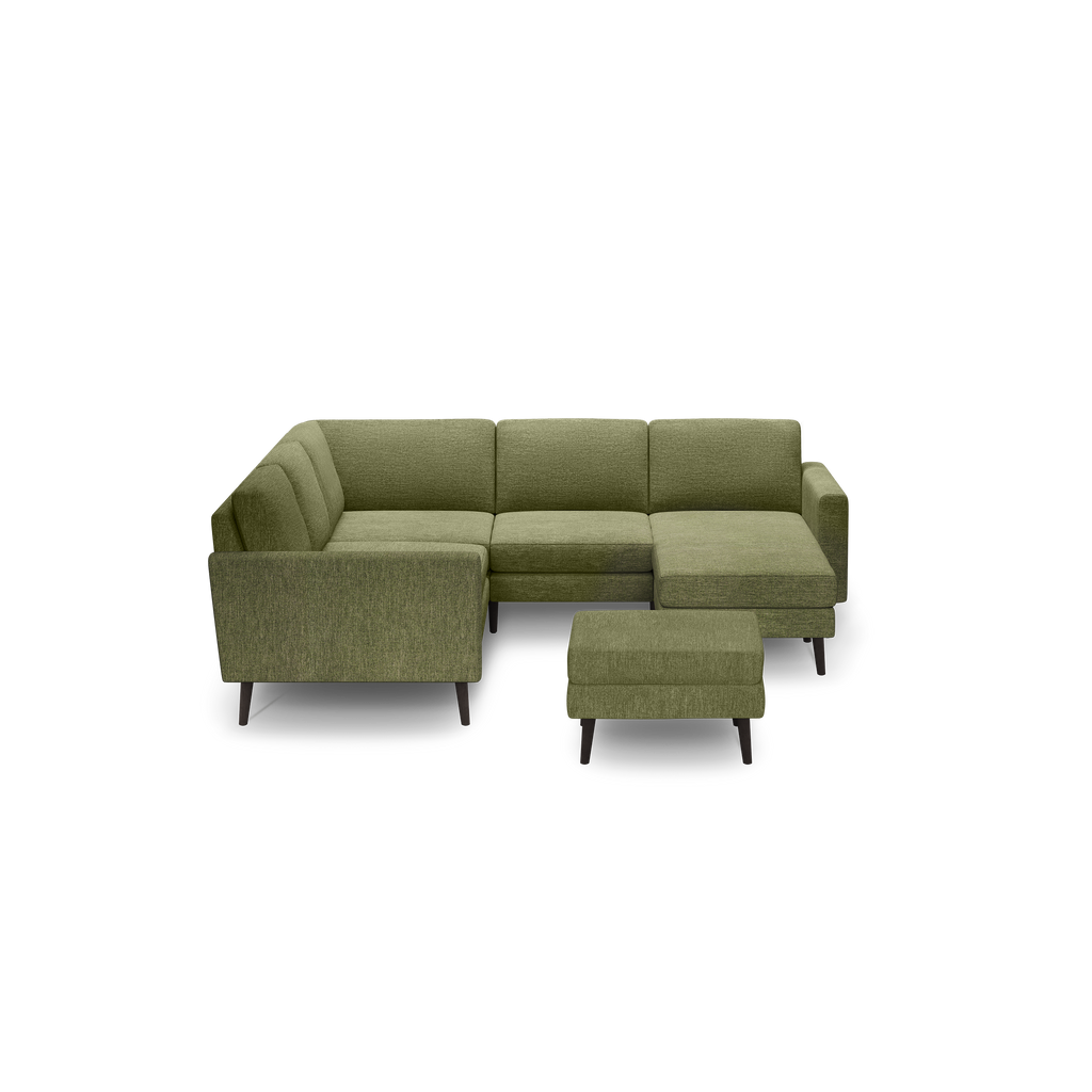 Green fabric L-shaped sectional sofa with tufted back cushions and matching ottoman on dark wooden legs, isolated on black background.
