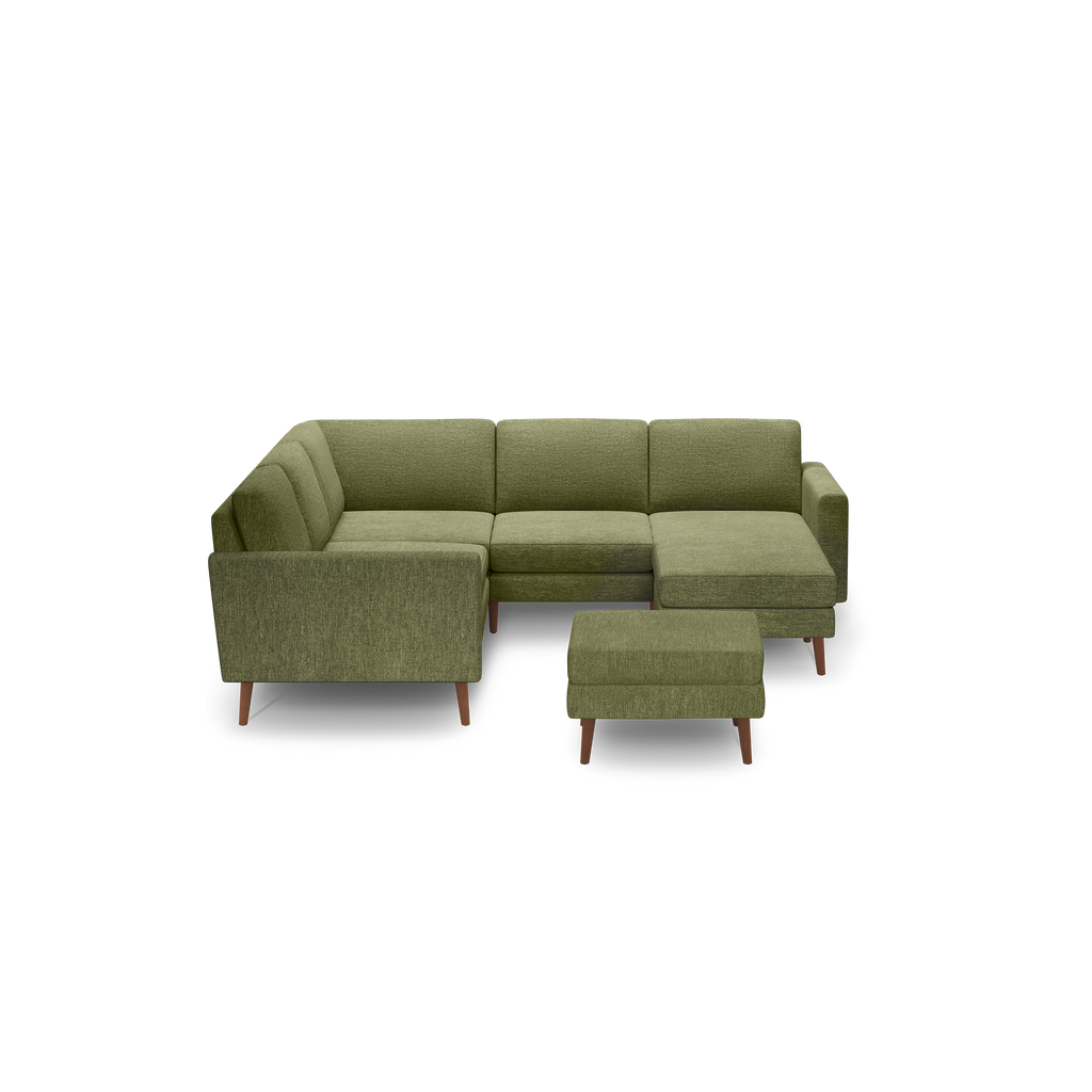 Green upholstered L-shaped sectional sofa with wooden legs and a matching ottoman on a black background.