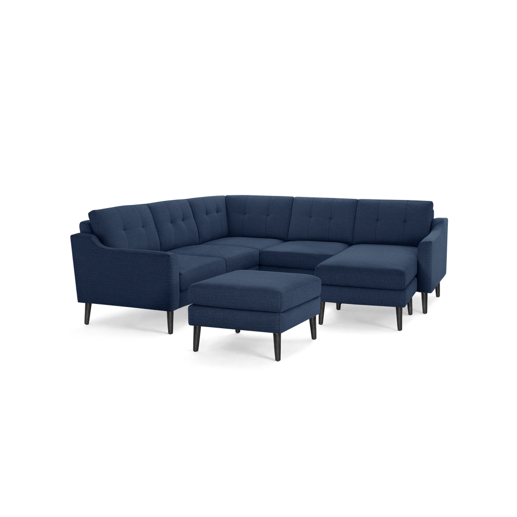 Modern navy blue fabric sectional sofa with tufted back cushions, angled armrests, and matching ottoman on black tapered legs.
