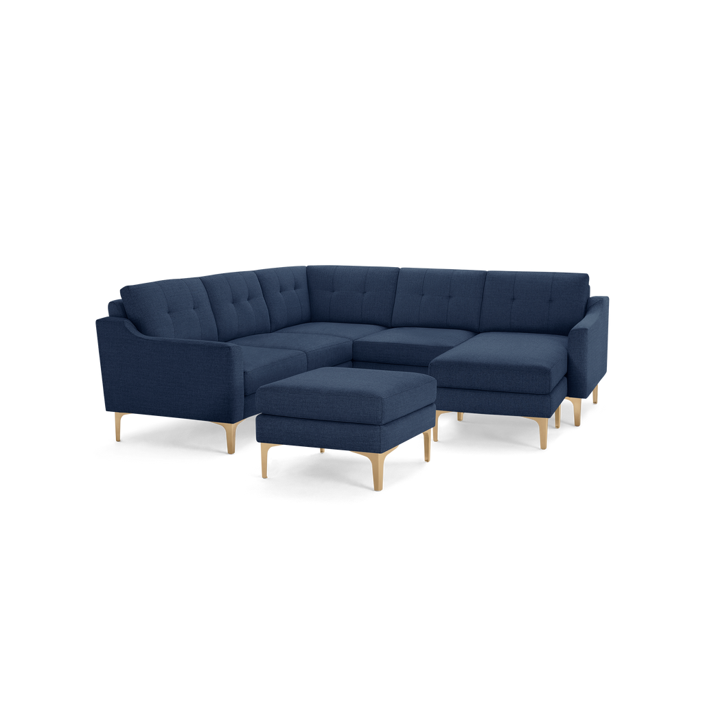 Modern navy blue fabric sectional sofa with tufted cushions, curved armrests, wooden legs, and matching ottoman.