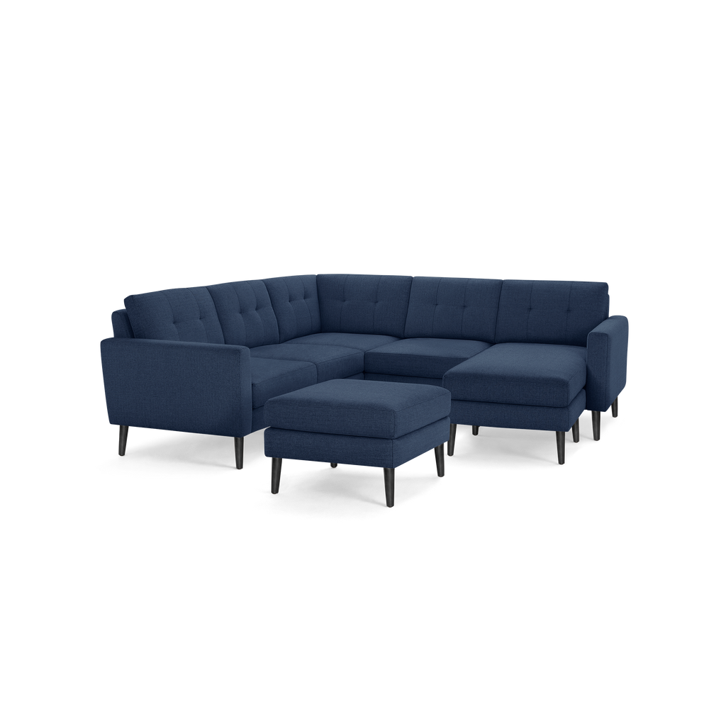 Mid-century modern navy blue fabric sectional sofa with black tapered wooden legs and matching ottoman.