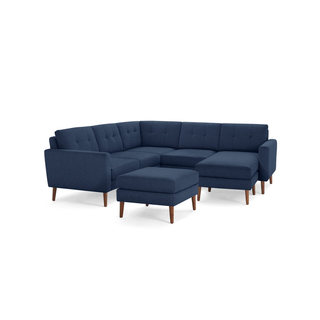 Navy blue L-shaped sectional sofa with tufted back cushions, wooden legs, and a matching upholstered ottoman.