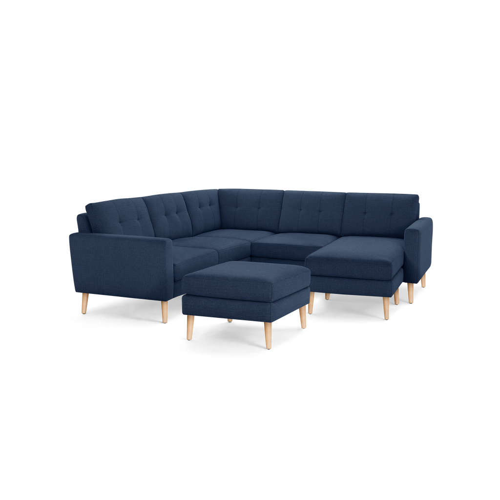 Modern navy blue fabric sectional sofa with tufted cushions and light wooden legs, including a matching ottoman.
