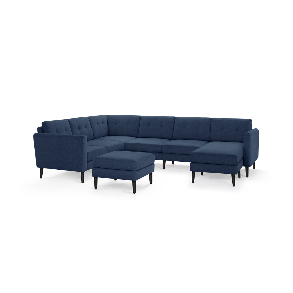 Navy blue L-shaped sectional sofa with tufted cushions, slim black legs, and a matching ottoman on a white background.