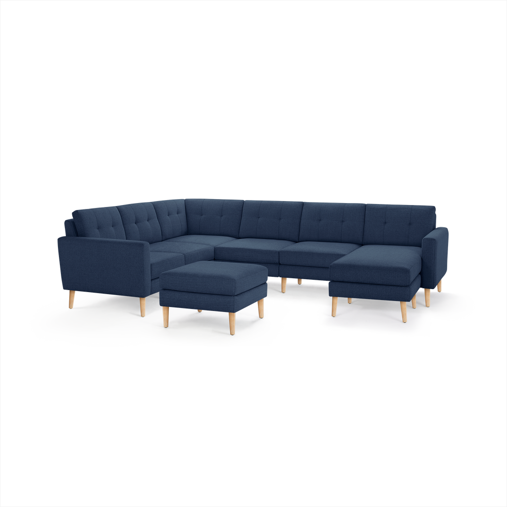 Modern navy blue L-shaped sectional sofa with tufted cushions and light wooden legs, accompanied by a matching square ottoman.
