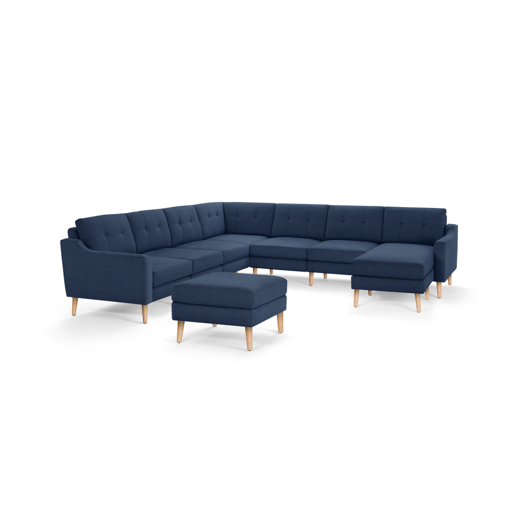 Modern navy blue fabric sectional sofa with tufted back cushions and light wooden legs, accompanied by matching ottoman.