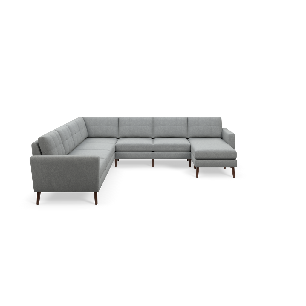 Gray modern sectional sofa with tufted cushions, wooden legs, and a chaise lounge on one end, isolated on black background.