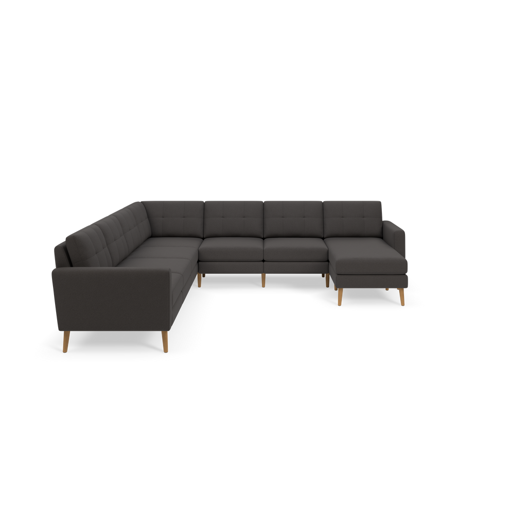 Dark gray L-shaped sectional sofa with tufted cushions and light wooden legs, set against black background.