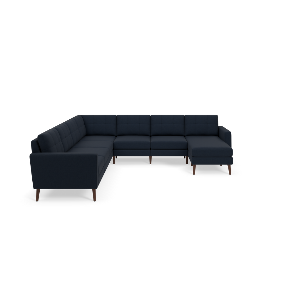 Dark blue L-shaped sectional sofa with tufted cushions and wooden legs isolated on black background.