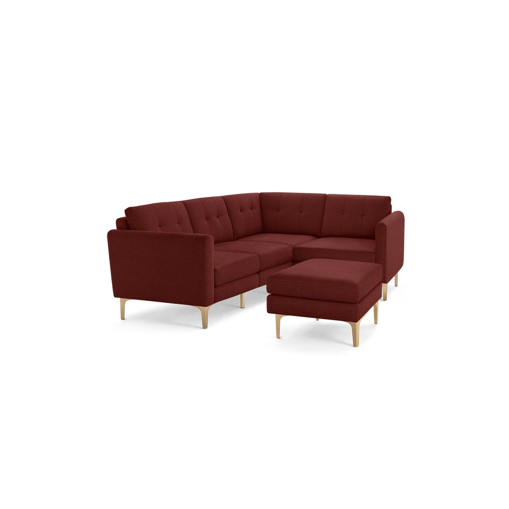 Modern L-shaped sectional sofa in deep red fabric with tufted back cushions and light wood legs, featuring a matching ottoman.