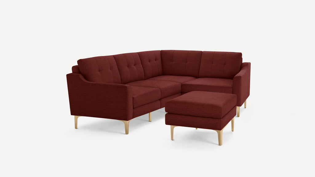 Modern L-shaped sectional sofa in deep red fabric with tufted cushions and light wooden legs, paired with a matching ottoman.