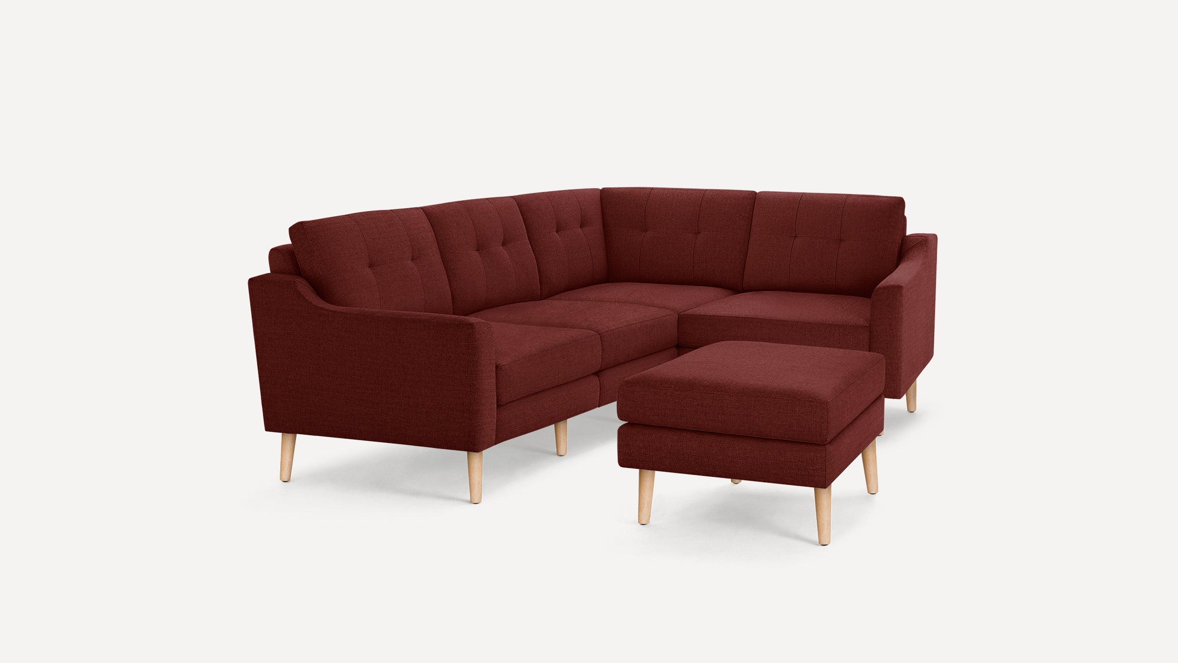 Modern L-shaped sectional sofa with tufted back cushions and matching ottoman, upholstered in deep red fabric with light wooden legs.