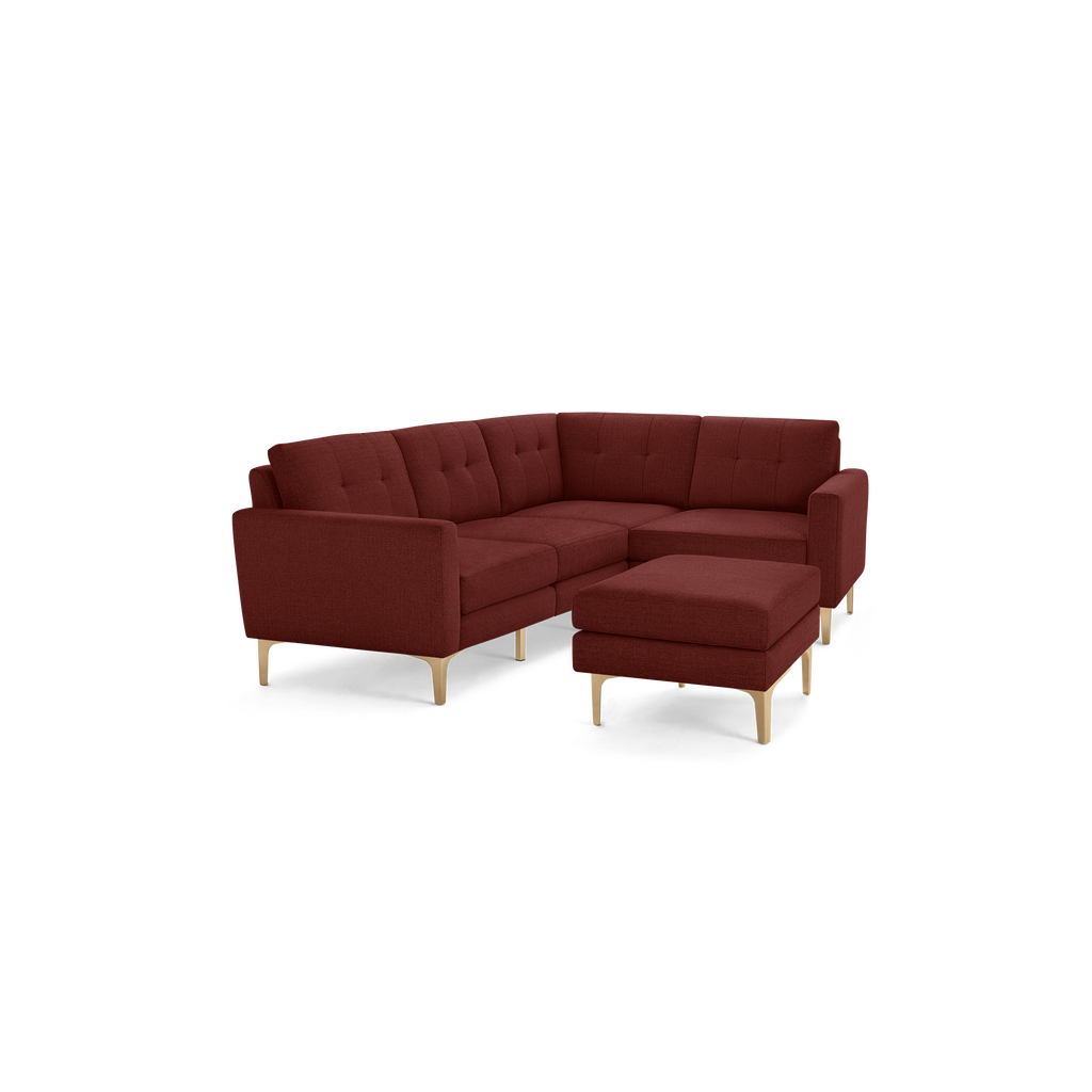 Modern L-shaped sectional sofa in deep red fabric with tufted cushions and light wooden legs, featuring a matching ottoman.