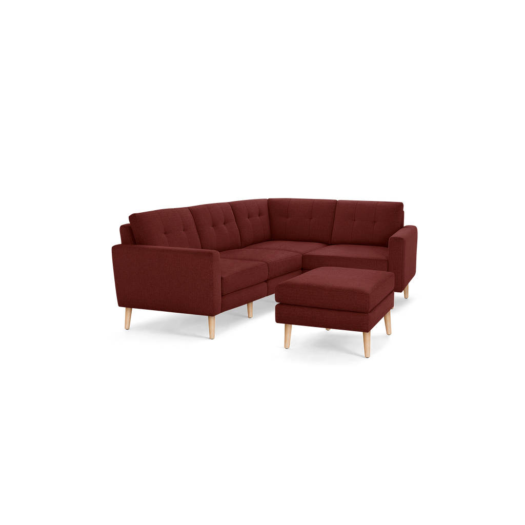 Maroon L-shaped sectional sofa with tufted cushions and wooden legs, featuring a matching square ottoman.