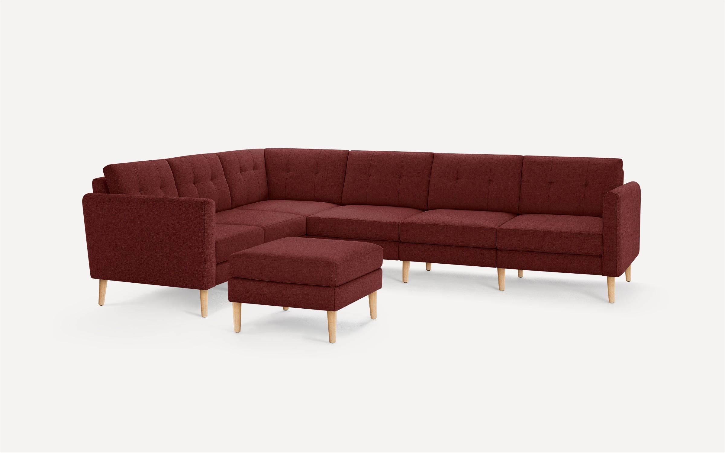 Modern maroon fabric L-shaped sectional sofa with tufted back cushions and light wooden legs, including matching ottoman.