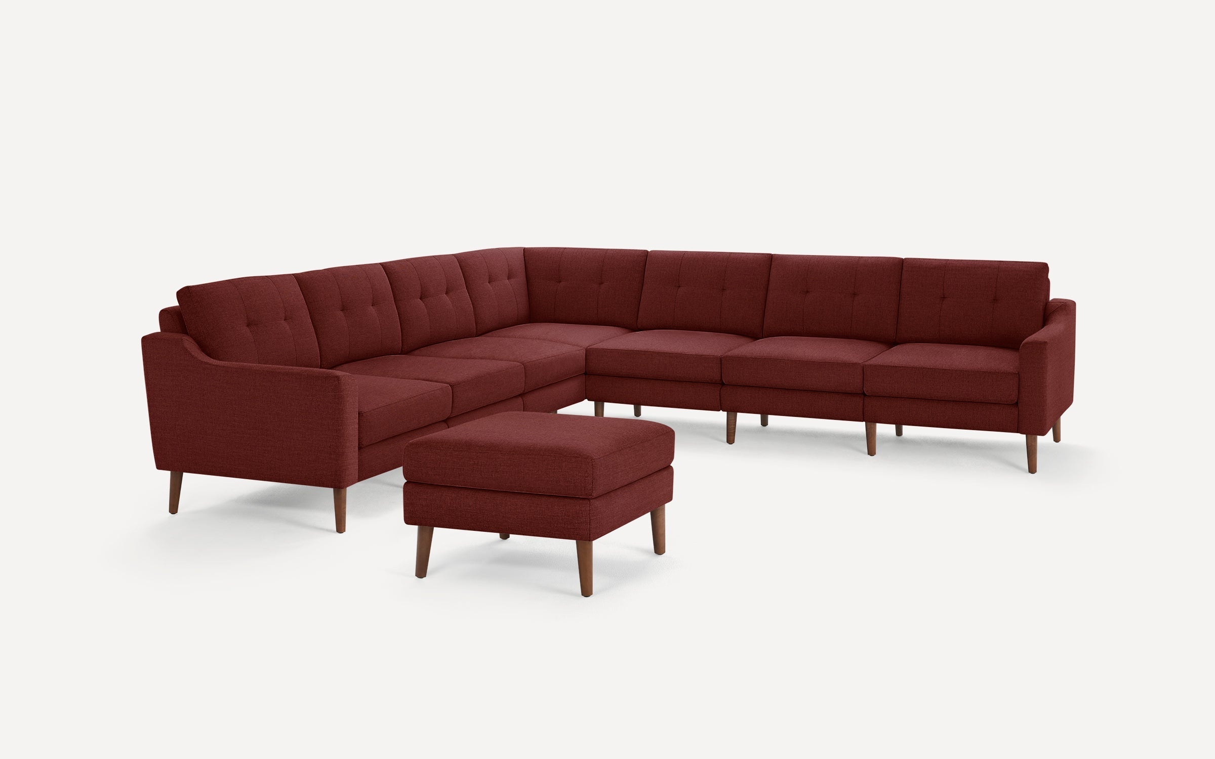 Deep red fabric upholstered L-shaped sectional sofa with tufted back cushions and matching square ottoman on wooden legs.