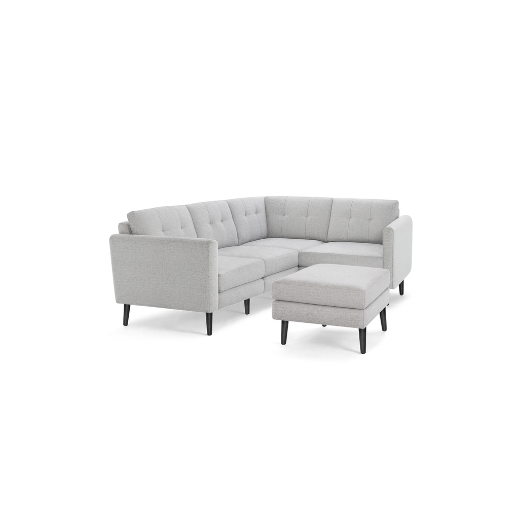 Light gray fabric L-shaped sectional sofa with tufted back cushions and matching ottoman, supported by dark wooden legs.