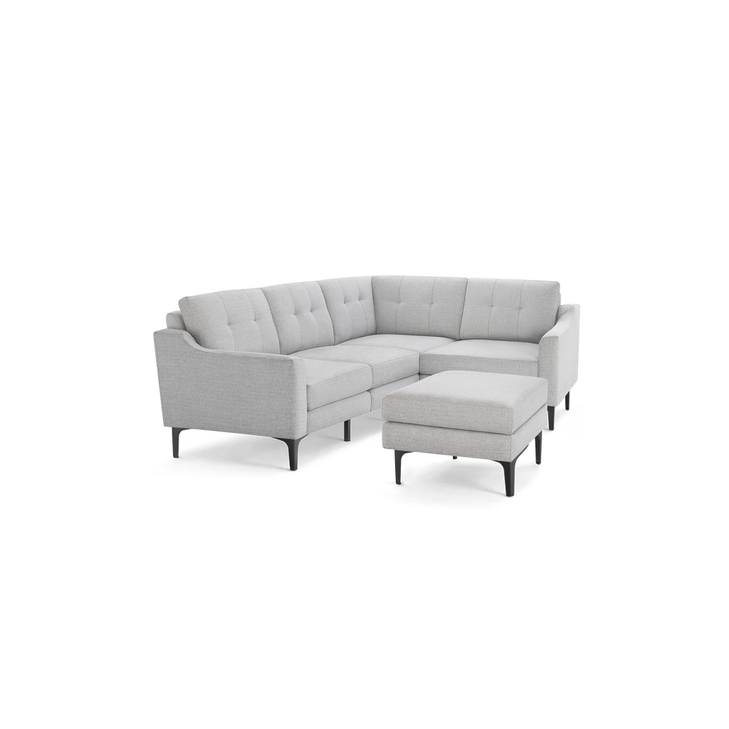 Light gray fabric L-shaped sectional sofa with tufted back cushions, slim black legs, and matching ottoman.