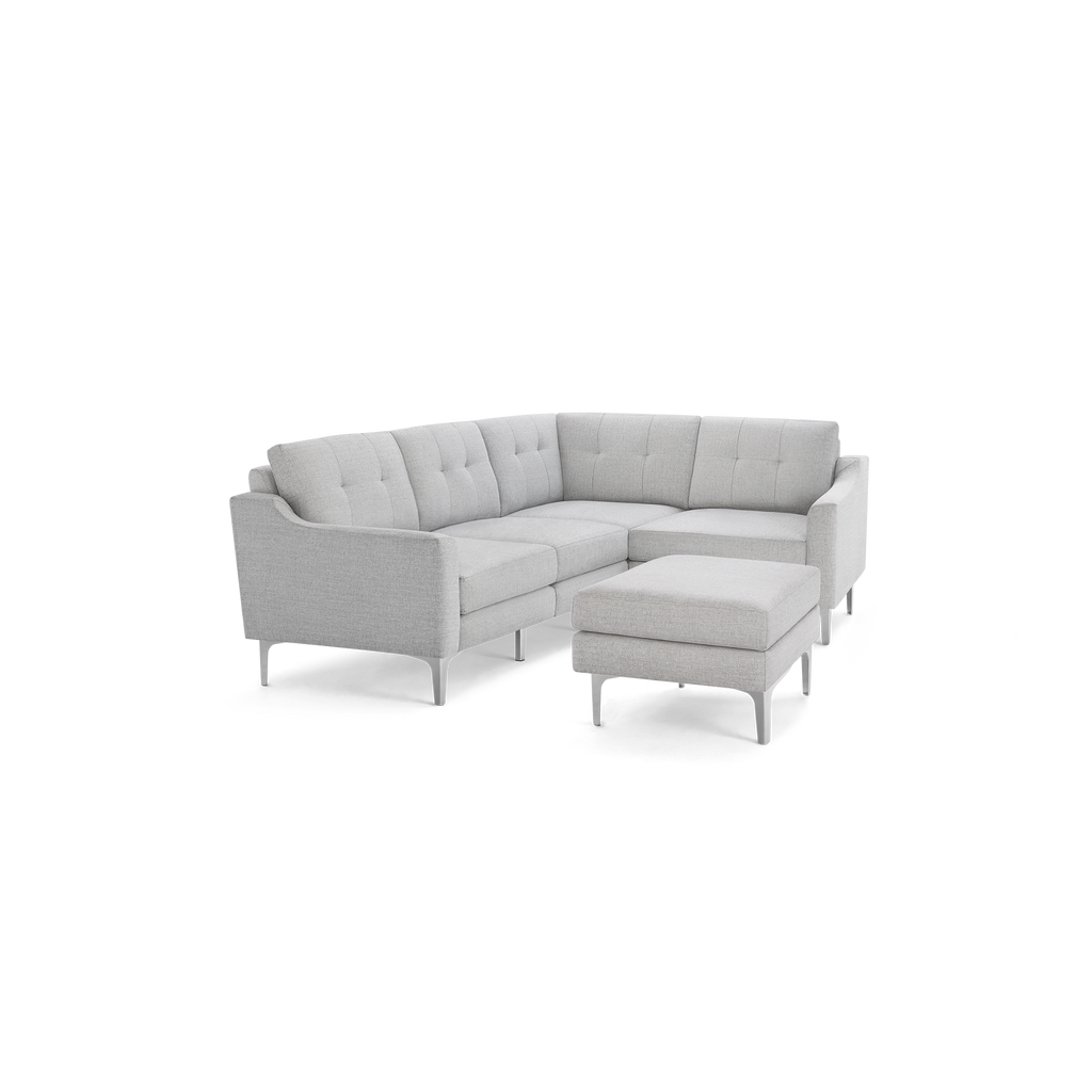 Light gray L-shaped sectional sofa with tufted back cushions and matching ottoman, supported by slender legs.