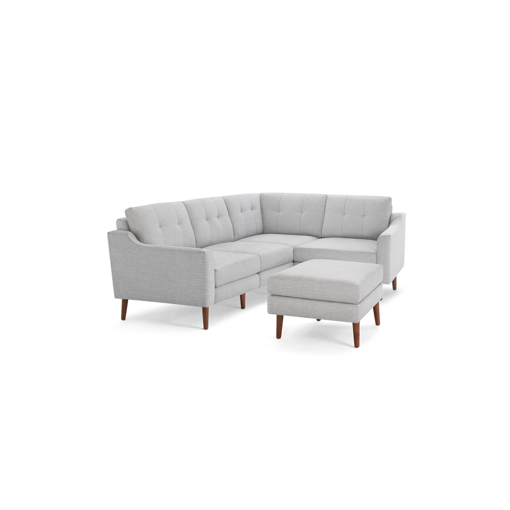 Light gray fabric sectional sofa with tufted cushions, wooden legs, and a matching ottoman, modern design.