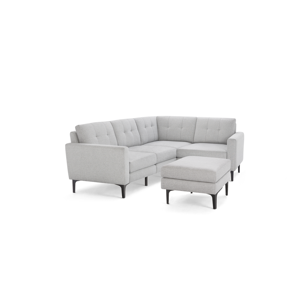 Light gray fabric sectional sofa with tufted back cushions and matching ottoman on slim black legs.