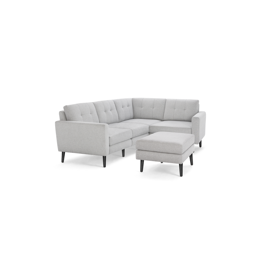 Light gray L-shaped sectional sofa with tufted cushions and matching ottoman, featuring black tapered wooden legs.