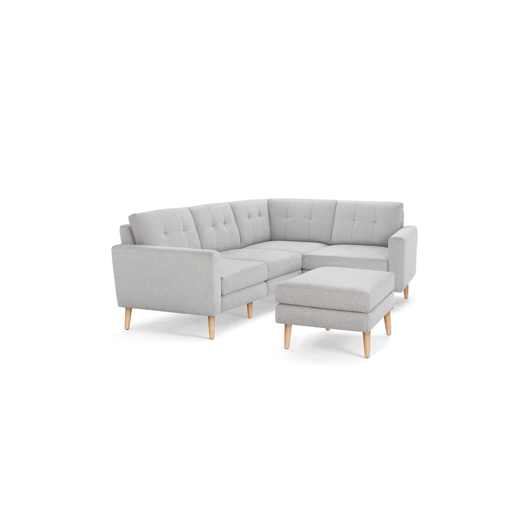 Light gray L-shaped sectional sofa with tufted back cushions and matching ottoman, supported by wooden legs.