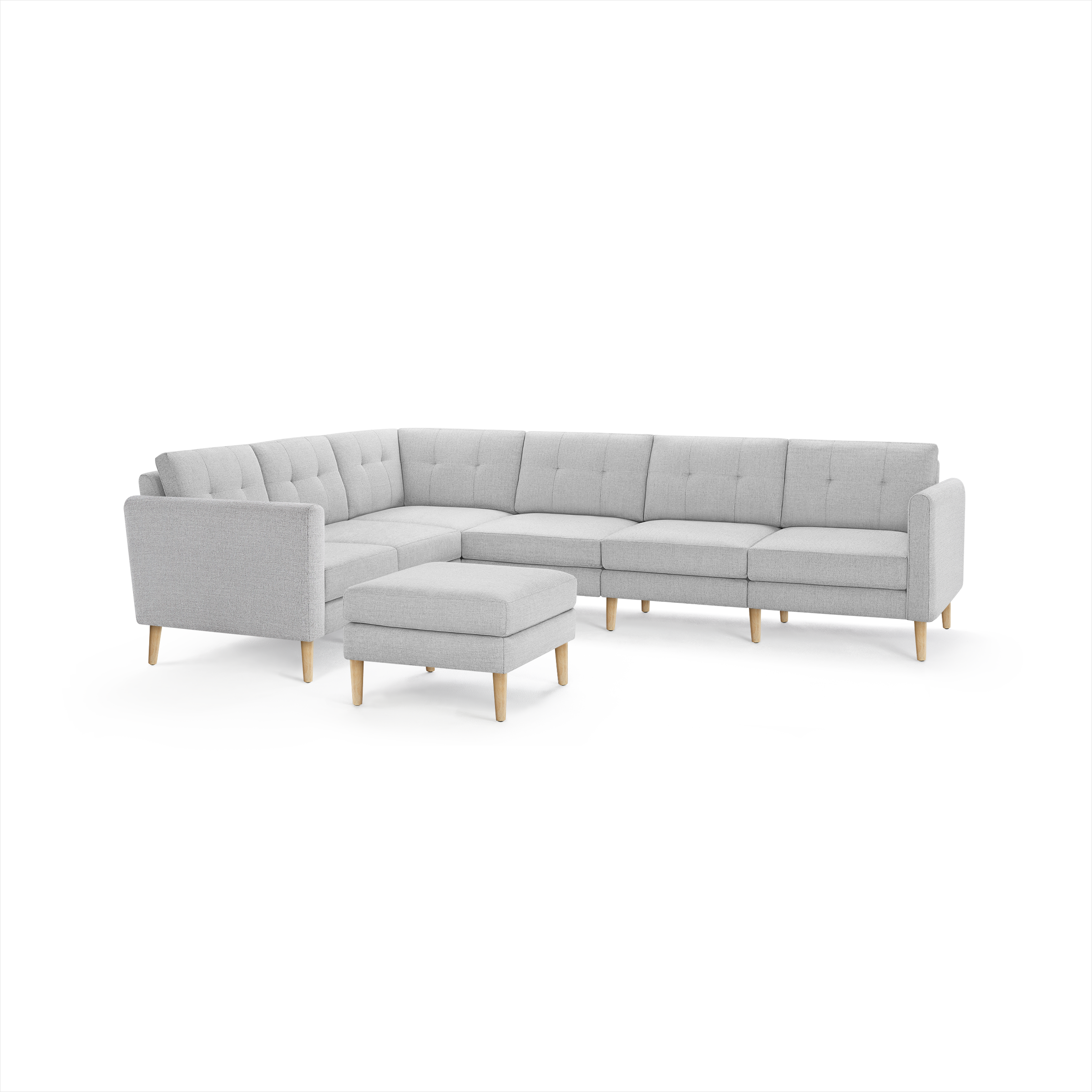 Light gray fabric sectional sofa with tufted back cushions and matching ottoman, supported by natural wooden legs.