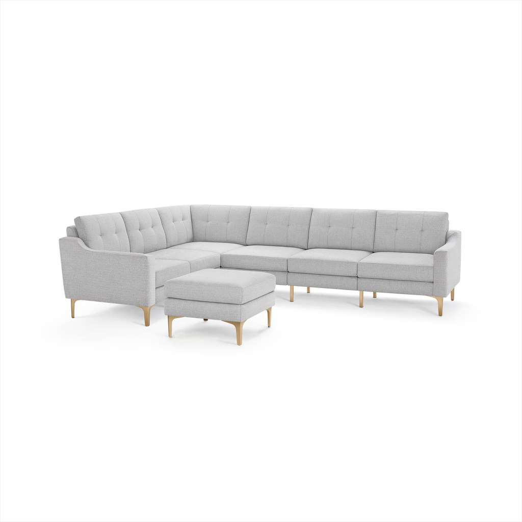Light gray upholstered L-shaped sectional sofa with tufted cushions and a matching ottoman, supported by light wooden legs.