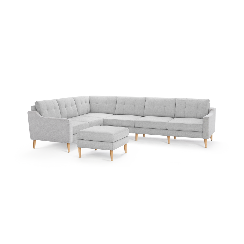Light gray upholstered L-shaped sectional sofa with tufted cushions and light wood legs, accompanied by a matching ottoman.