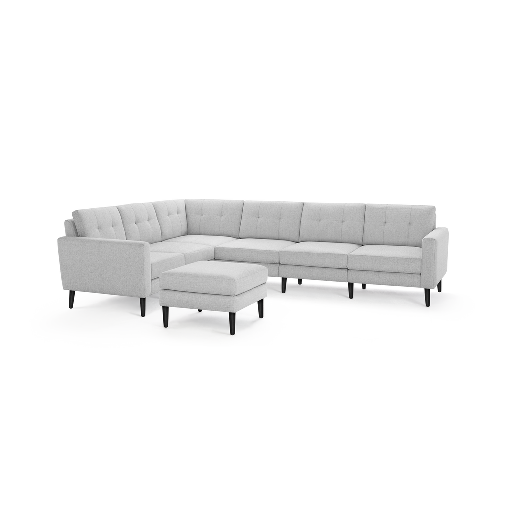 Light gray fabric L-shaped sectional sofa with tufted back cushions and matching ottoman on black wooden legs.