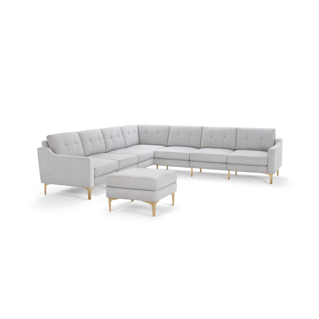 Light gray fabric L-shaped sectional sofa with tufted back cushions and matching ottoman, featuring wooden legs.