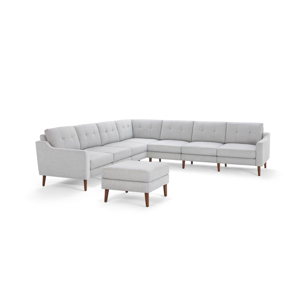 Light gray fabric sectional sofa with tufted back cushions and matching ottoman, featuring wooden legs and modern design.