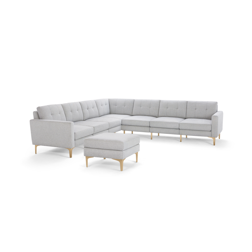 Light gray fabric L-shaped sectional sofa with tufted back cushions and matching ottoman, wooden legs.