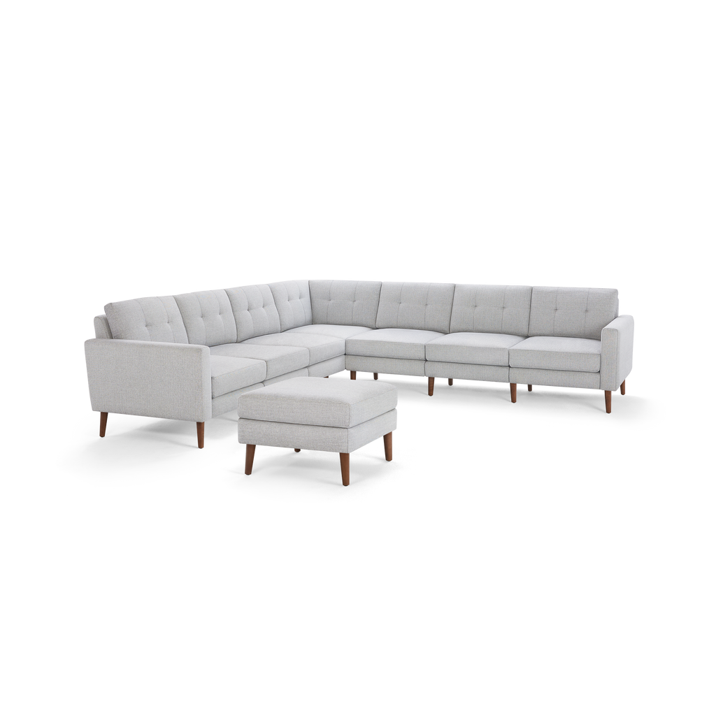 Light gray fabric sectional sofa with tufted back cushions, wooden legs, and a matching cushioned ottoman.