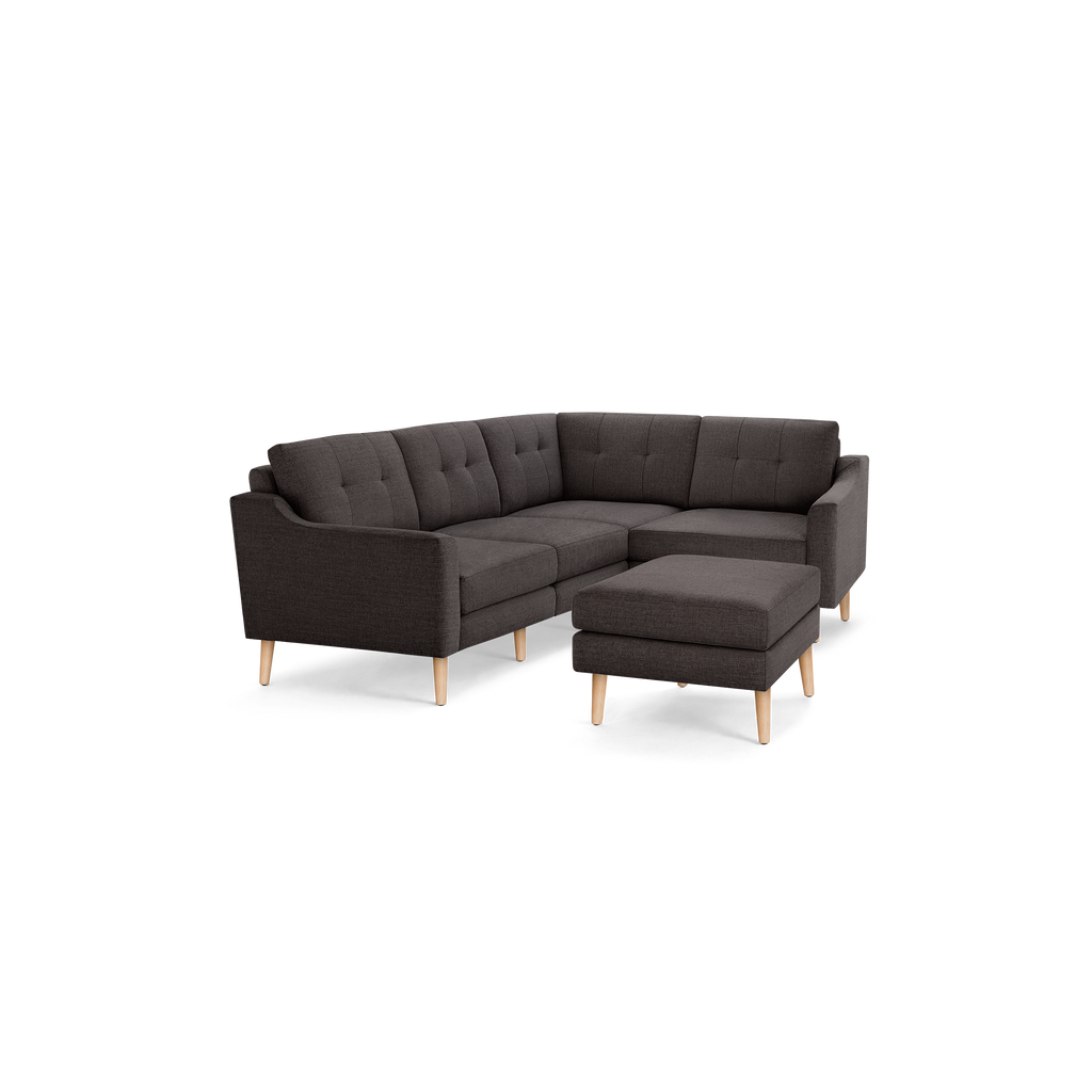Dark gray fabric tufted L-shaped sectional sofa with angled wooden legs and matching ottoman on black background.