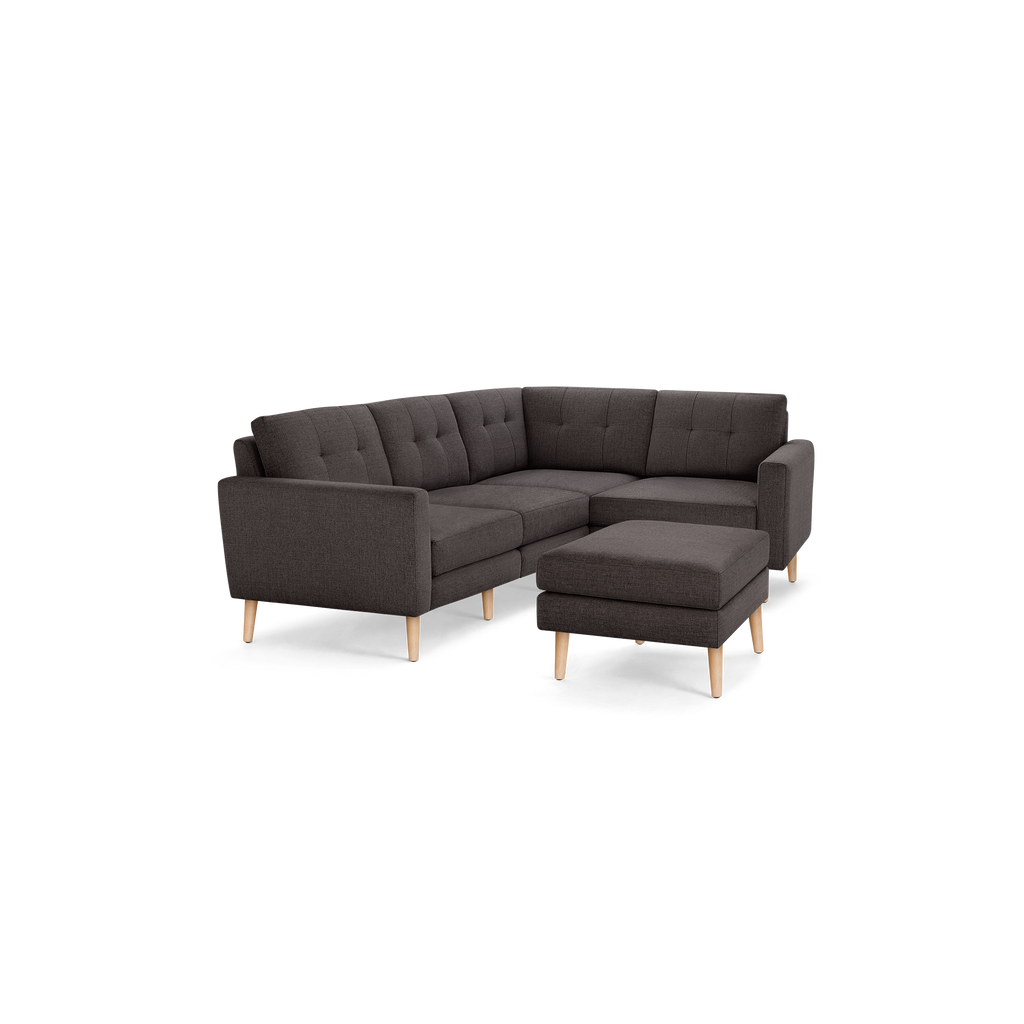 Dark gray L-shaped sectional sofa with tufted cushions and light wooden legs, including a matching ottoman.