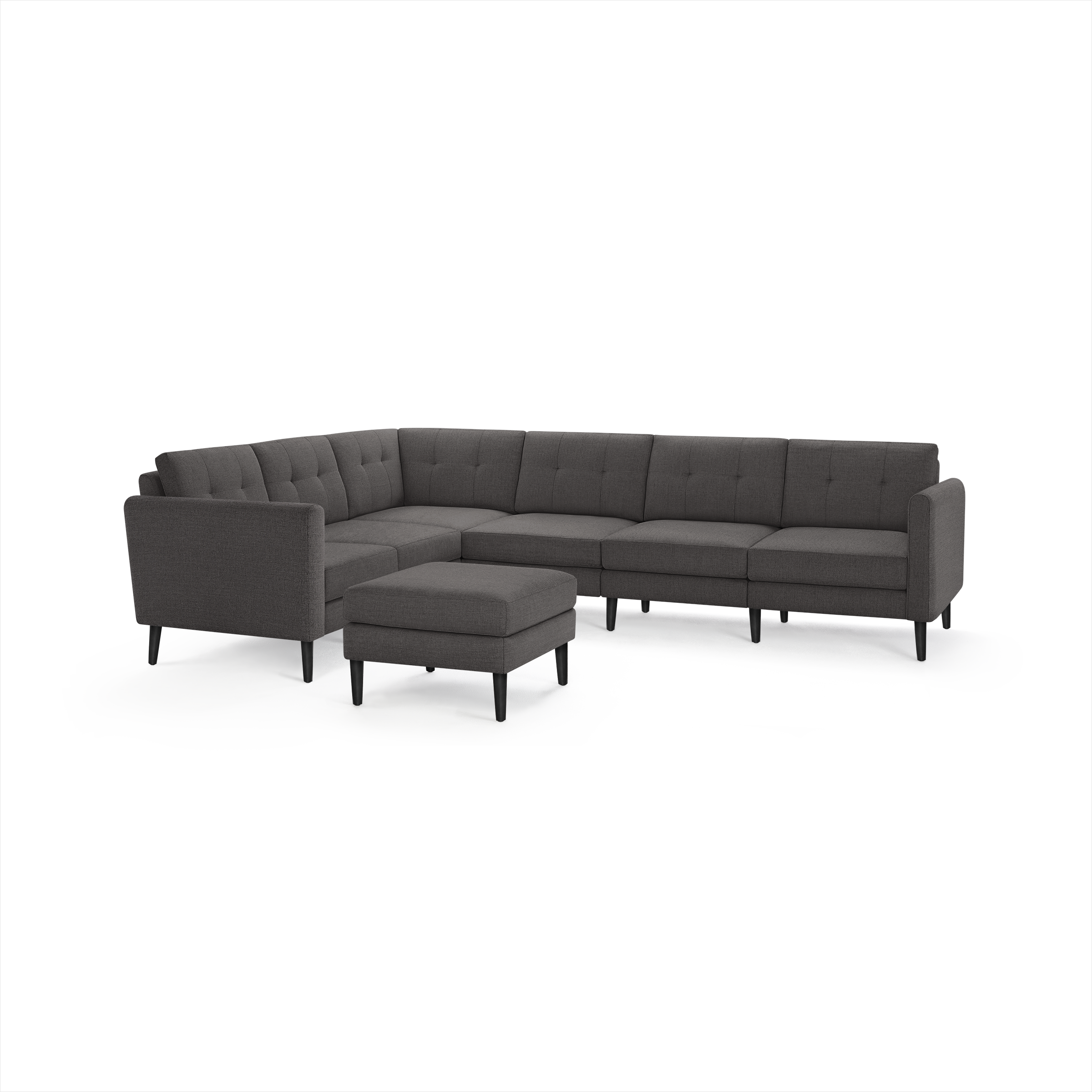 Dark gray fabric sectional sofa with tufted cushions, L-shaped design, and matching ottoman, featuring slim black legs.