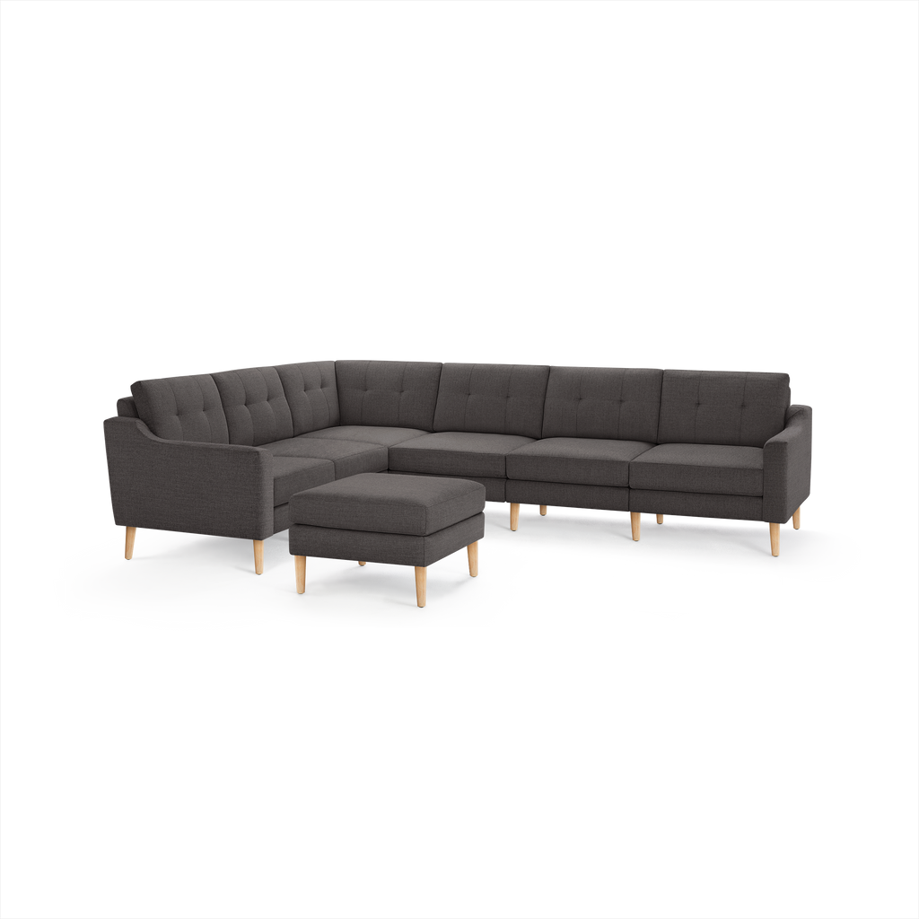 Dark gray fabric L-shaped sectional sofa with tufted cushions and matching ottoman, supported by light wooden legs.