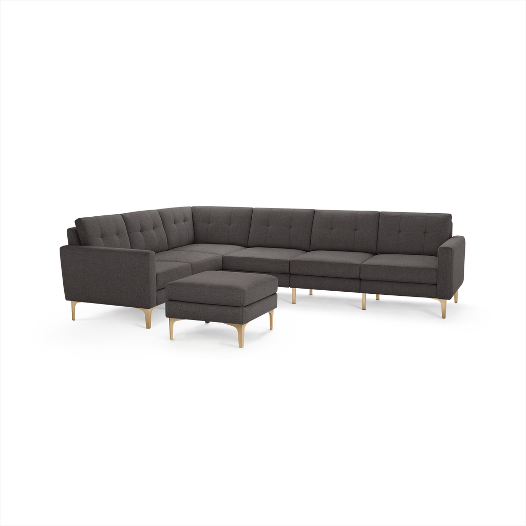 Dark gray modern sectional sofa with tufted cushions, light wooden legs, and matching ottoman on white background.