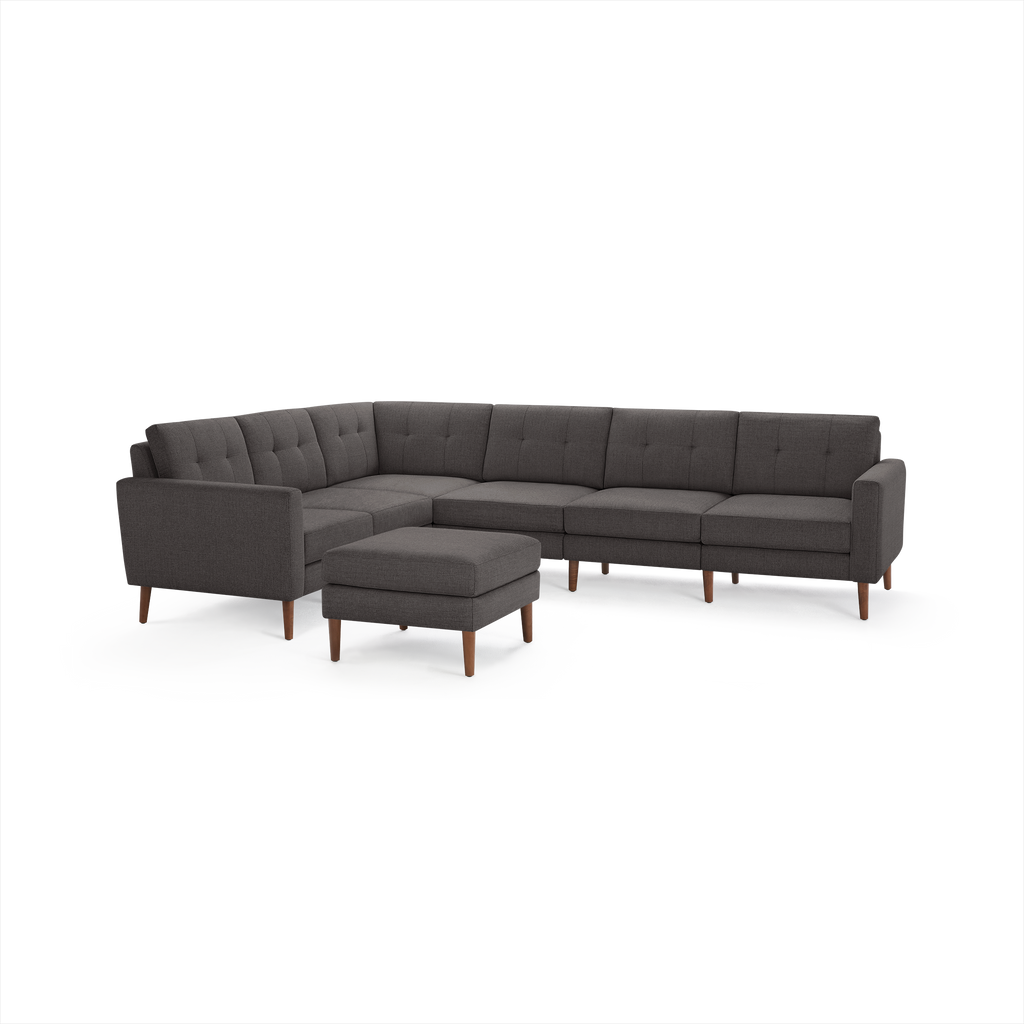 Dark gray L-shaped sectional sofa with tufted cushions and matching ottoman, supported by wooden legs.